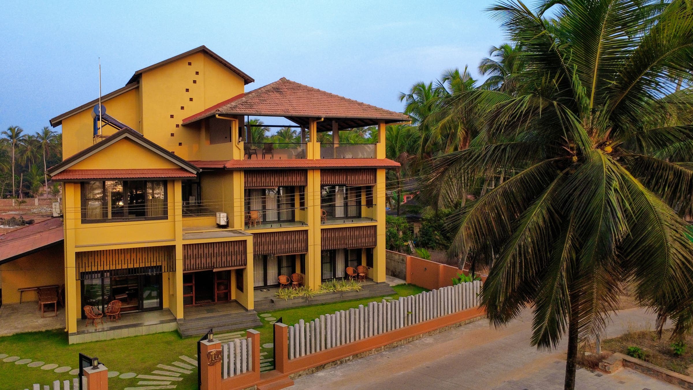 The villa at dusk, its balconies lit and coconut palms alongside