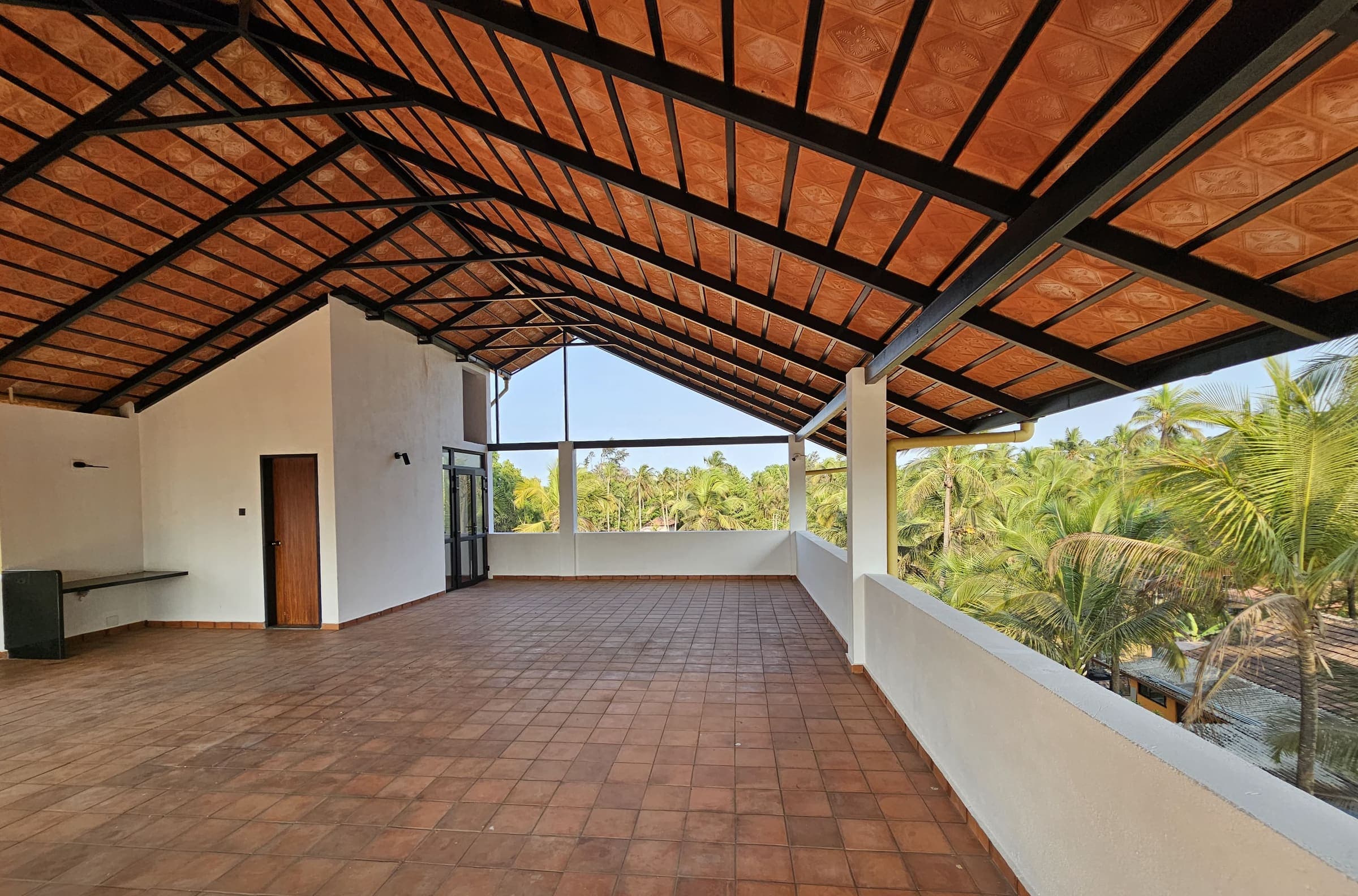 The open rooftop terrace under a tiled roof, looking over coconut palms